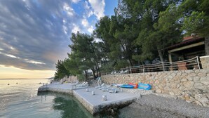 Une jetée en pierre, agrémentée de chaises longues et d’un radeau gonflable bleu, surplombe une étendue d’eau bordée d’arbres et d’un mur de pierre.