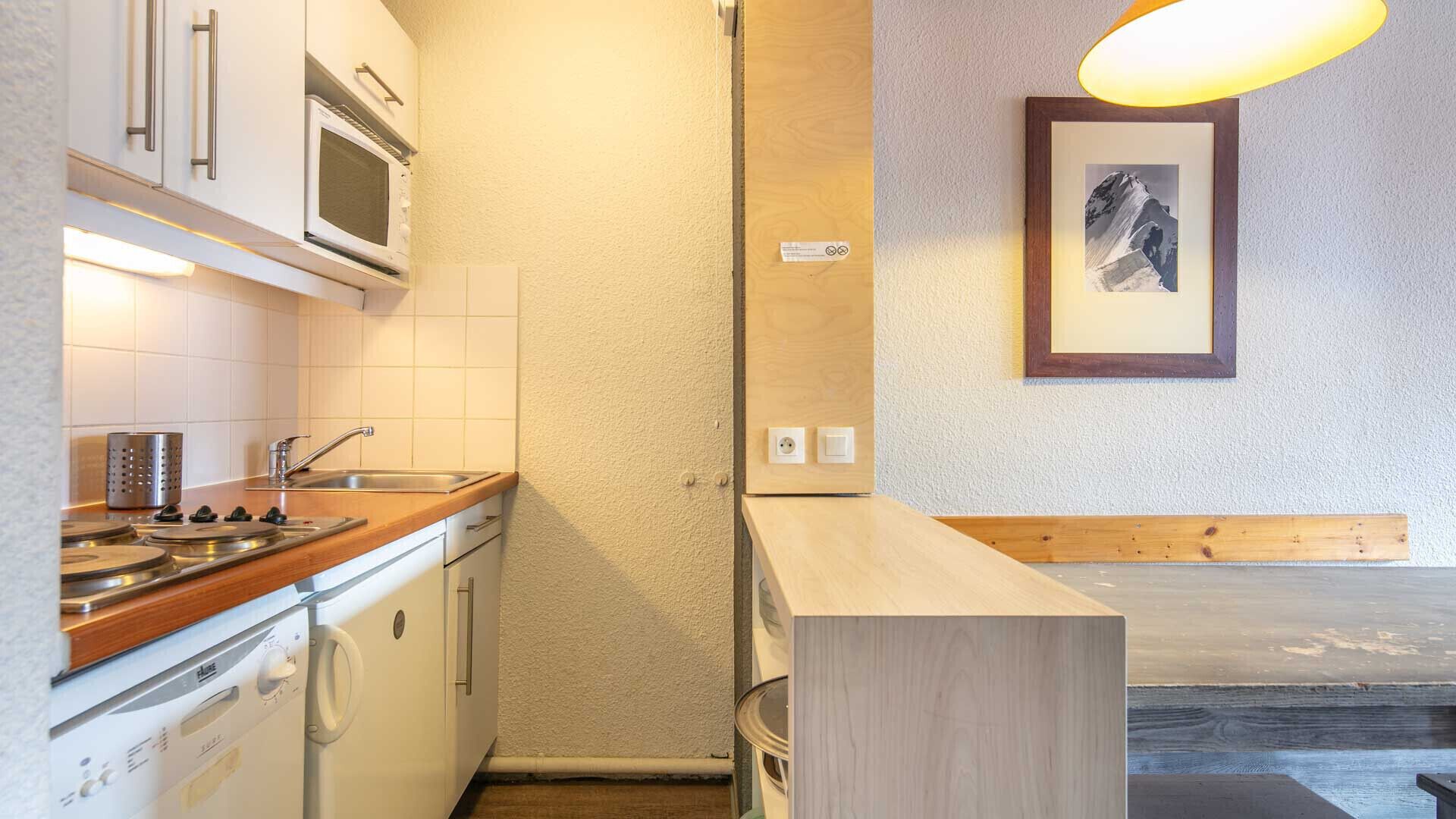 Une cuisine compacte équipée d’un four à micro-ondes, d’une cuisinière et d’un évier. On y trouve un banc en bois et un tableau encadré accroché au mur.