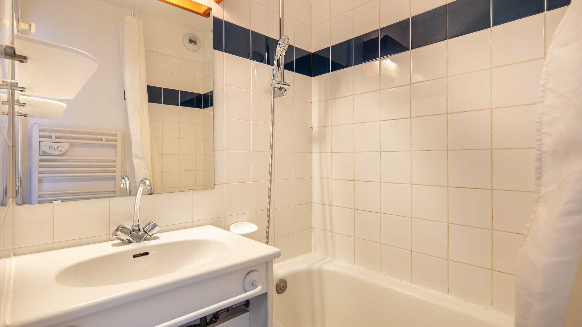 Une salle de bain avec un lavabo blanc, un miroir et une douche.