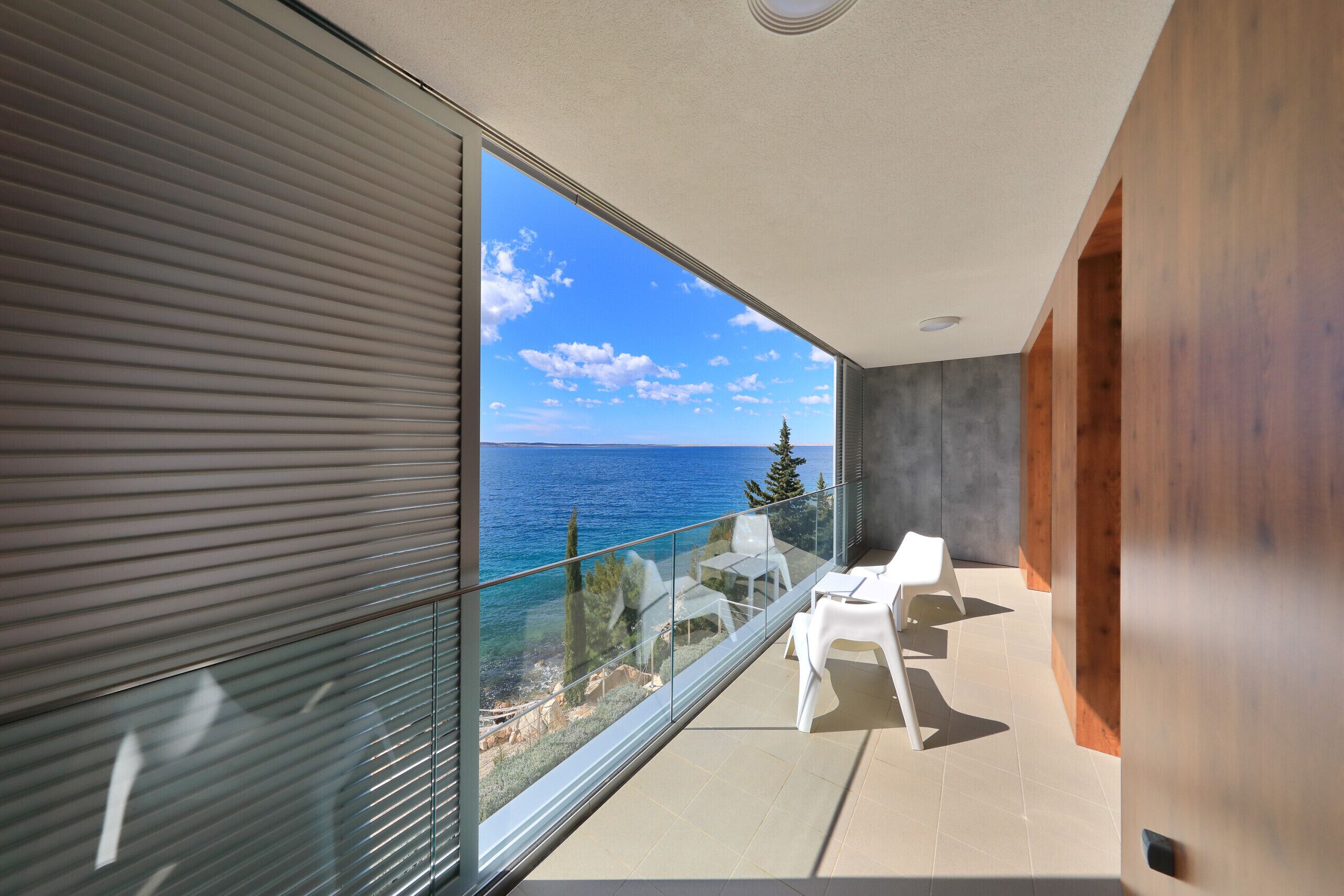 Un balcon avec vue sur la mer, des chaises blanches et un intérieur moderne.