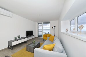 Ein modernes Wohnzimmer mit einer Couch, einem Couchtisch, einem Fernseher und einem großen Fenster mit Blick.