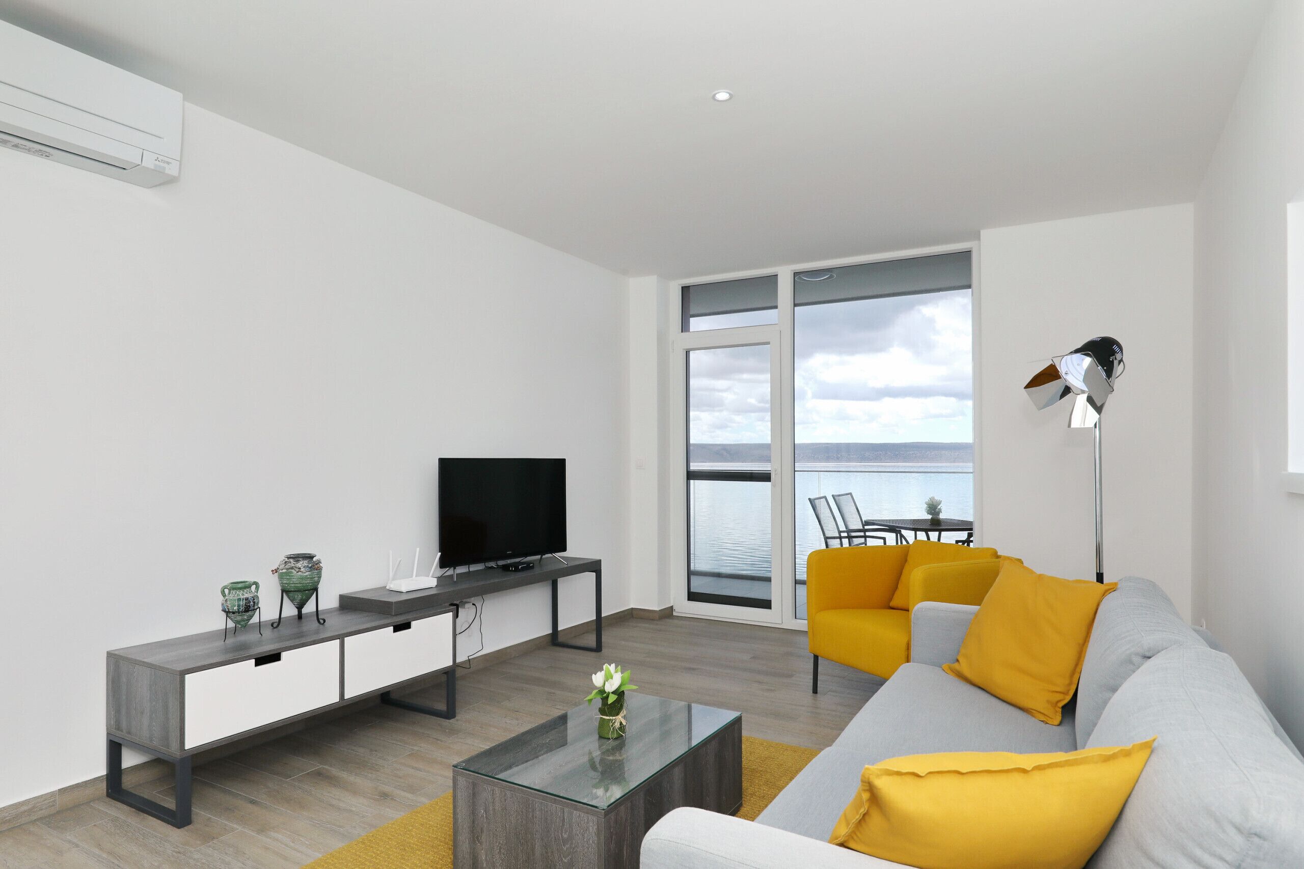 A modern living room with a sofa, coffee table, TV, and a balcony with a view.