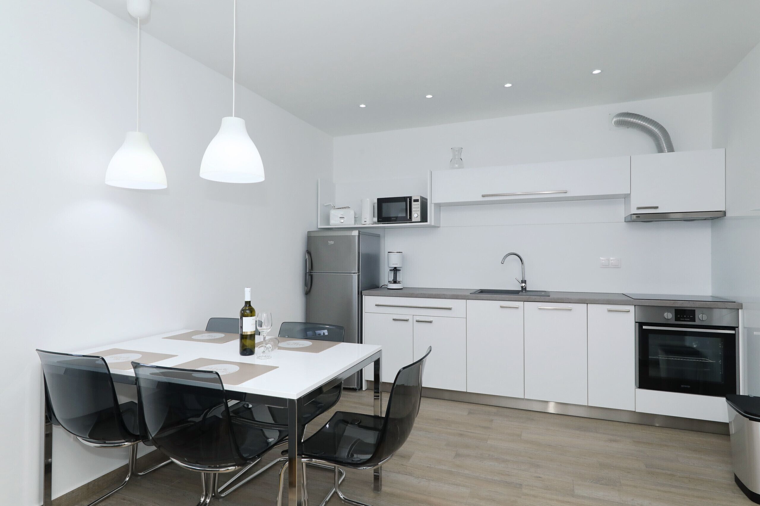 A modern kitchen with white cabinets, stainless steel appliances, and black chairs around a white table.