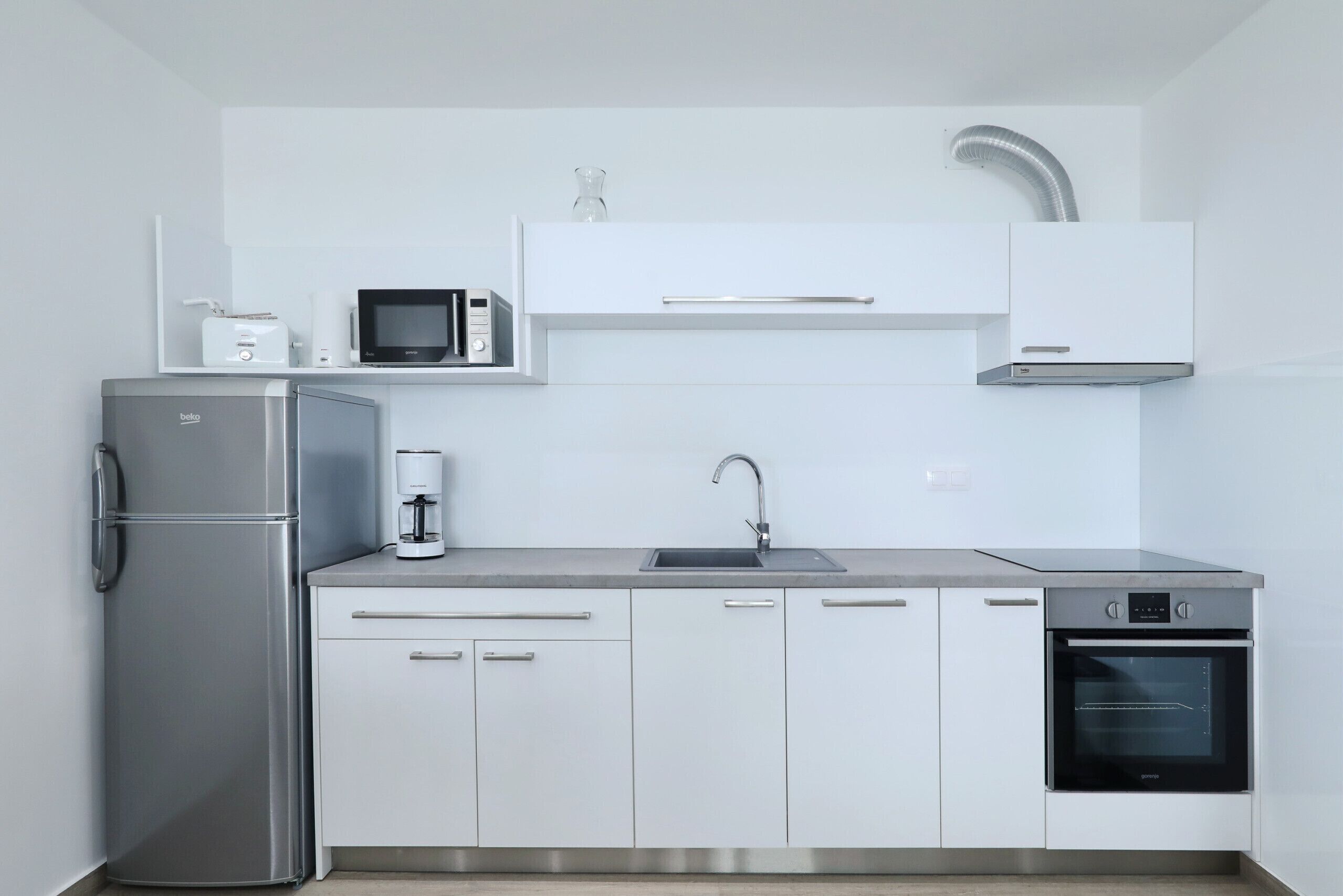 A modern kitchen with a refrigerator, microwave, coffee maker, sink, cabinets, and an oven.