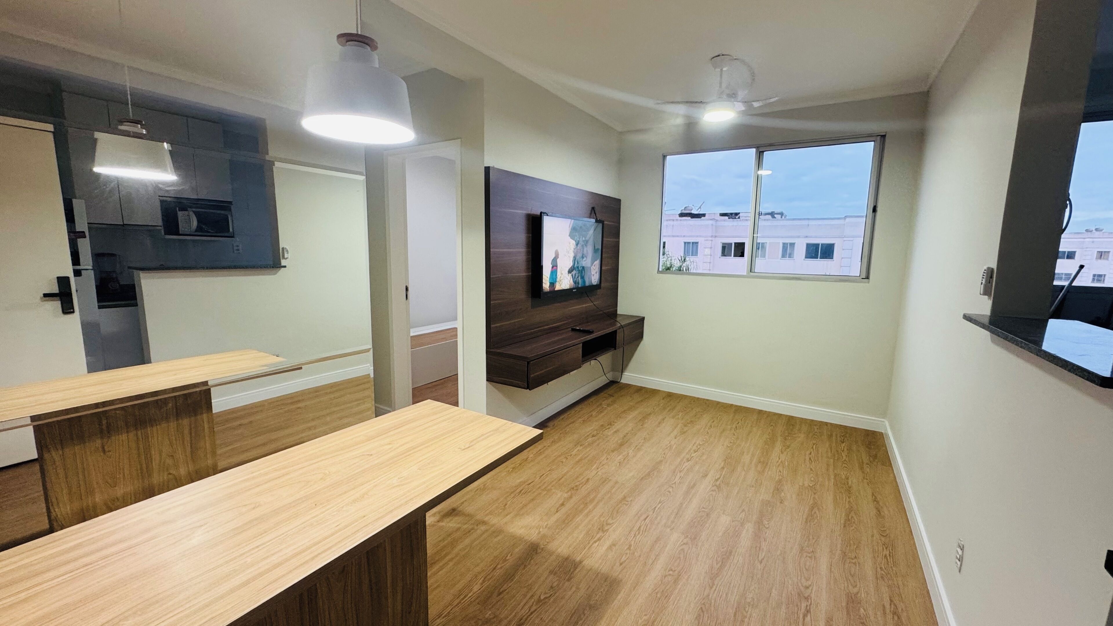 Een moderne keuken met ingebouwde apparatuur, een houten eettafel en een aan de muur bevestigde televisie.