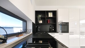 A modern kitchen with a black countertop, white cabinets, a built-in oven, and a window with a view. - Villa Astur with Private Pool (Zemunik Gornji)