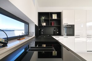 A modern kitchen with a black countertop, white cabinets, a built-in oven, and a window with a view. - Villa Astur with Private Pool (Zemunik Gornji)