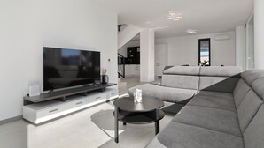 A modern living room with a flat-screen TV, a grey sofa, and a small round table. - Villa Astur with Private Pool (Zemunik Gornji)