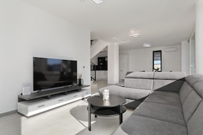 A modern living room with a flat-screen TV, a grey sofa, and a small round table. - Villa Astur with Private Pool (Zemunik Gornji)