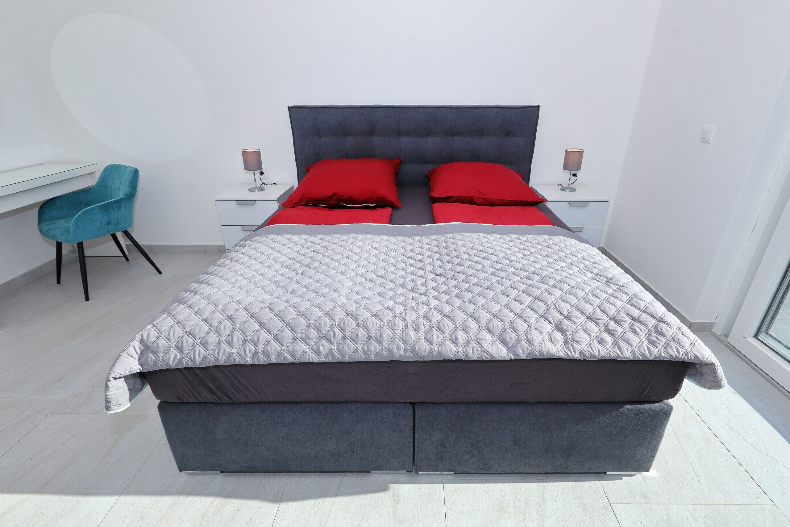 A modern bedroom with a large bed, two bedside tables, a desk, and a chair.