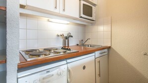 Una cocina compacta con armarios blancos, un microondas, una estufa con cuatro hornillas, un lavabo y un lavavajillas.