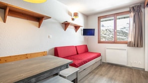 Ein Zimmer mit einer hölzernen Bank, einem roten Sofa, einem Wand-Fernseher und einem Fenster mit Blick auf schneebedeckte Berge.