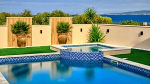 Ein Swimmingpool mit blau mosaikbesetztem Rand, umgeben von grünem Kunstrasen und Topfpflanzen.
