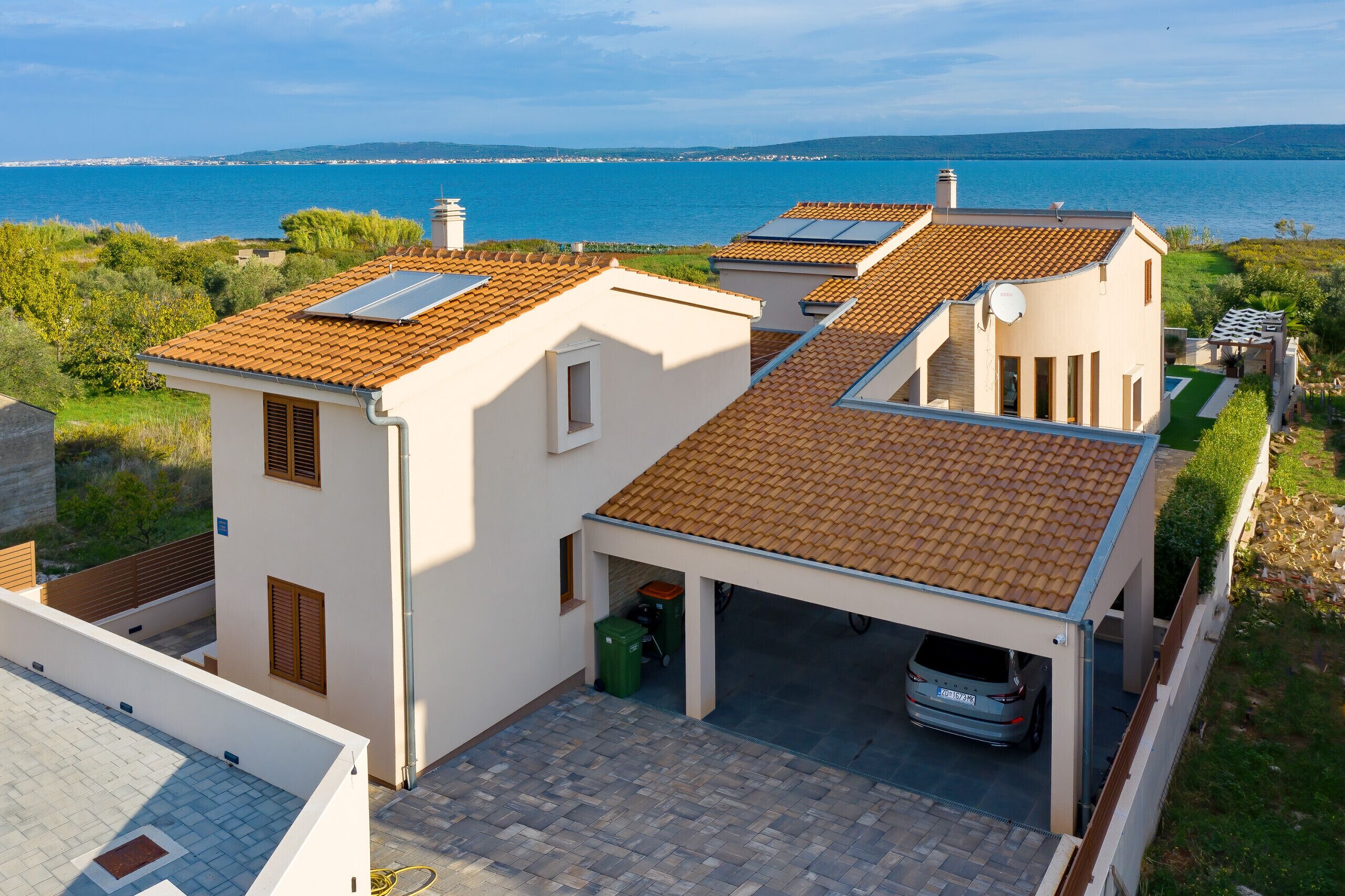 A residential building with a tiled roof, a car parked in a covered garage, and a view of the sea.