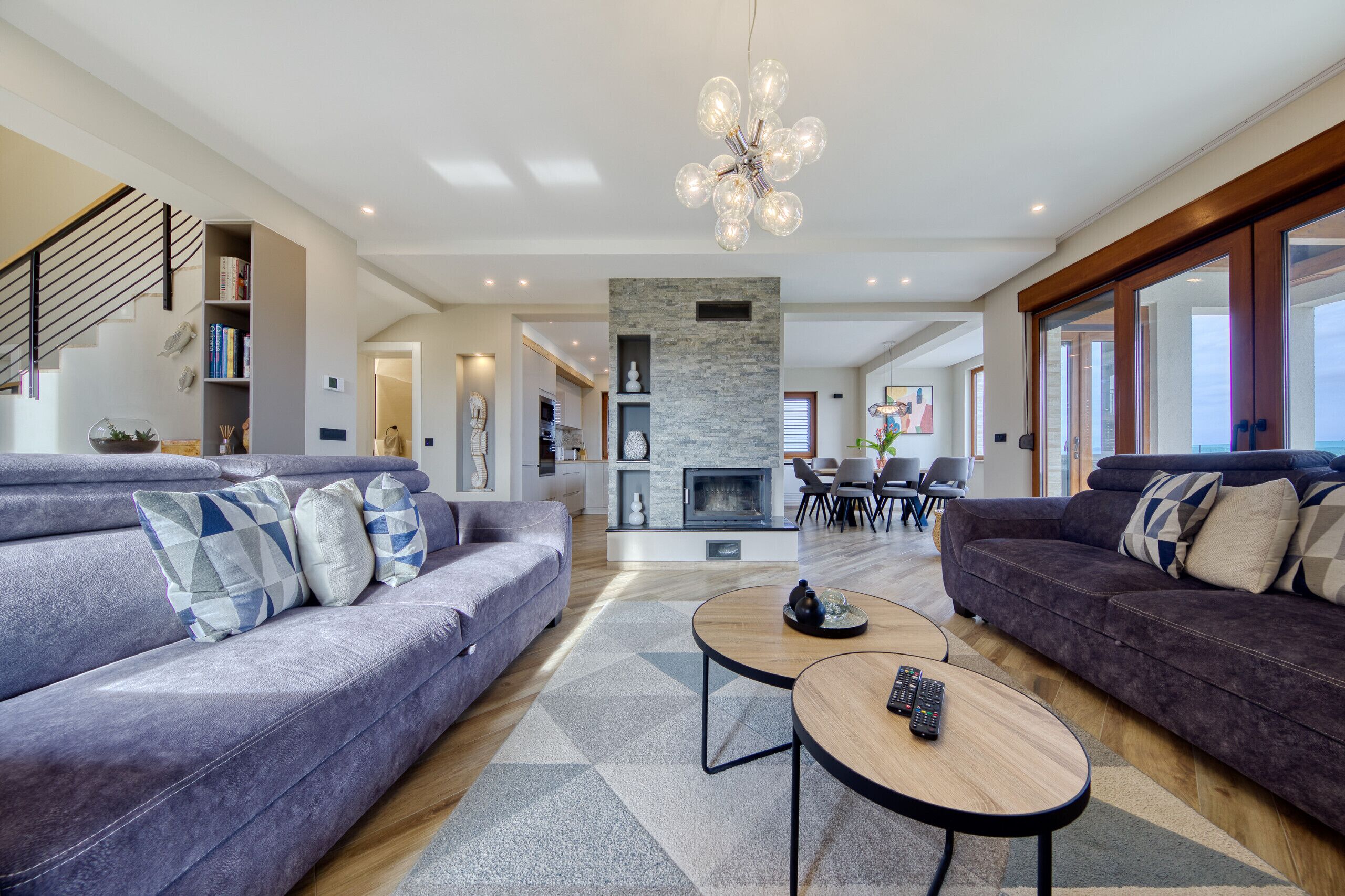 A modern living room with a fireplace, two sofas, a coffee table, and a staircase.