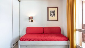 A bed with red bedding, a wall-mounted lamp, and a framed picture on the wall. - Charming studio for 4 people, with a balcony and a view of the ski slope (Tignes)