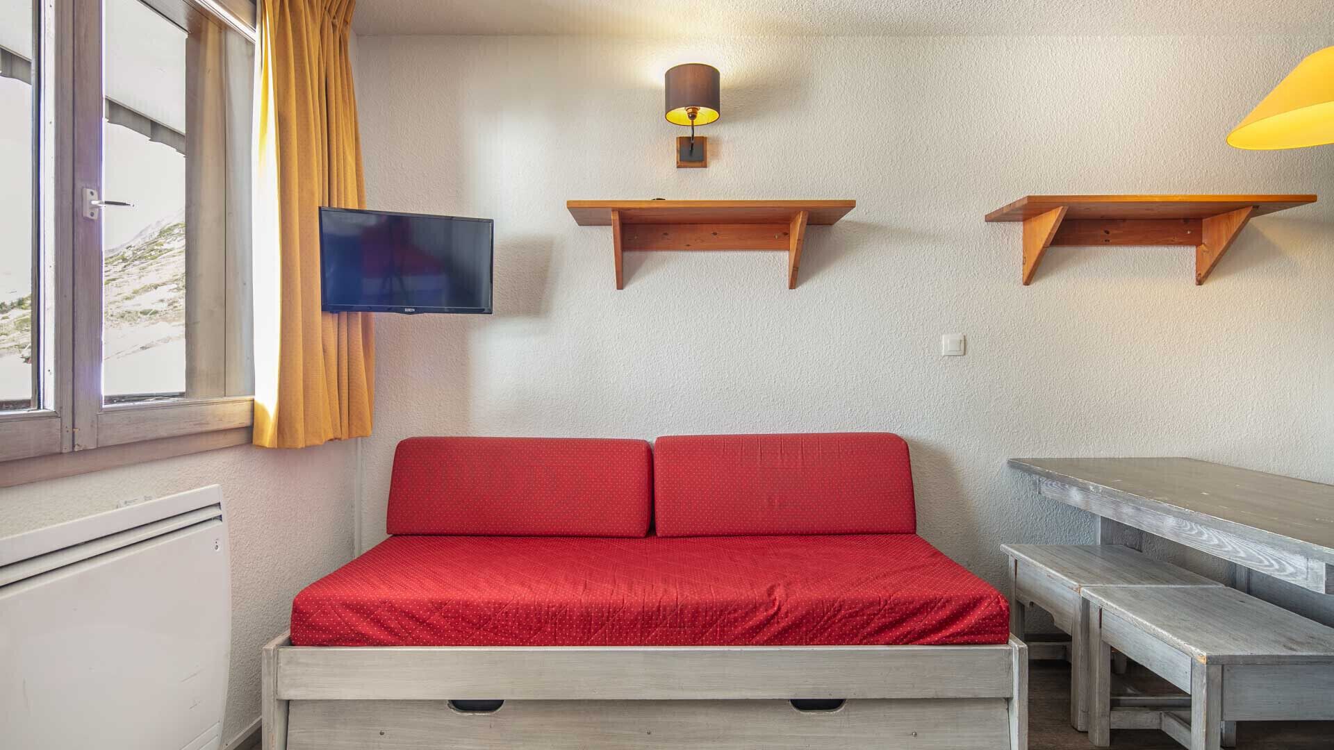 Una habitación con cama, televisor, estanterías de madera y ventana con cortinas.