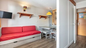A compact room with a sofa, a small table, a TV mounted on the wall, and a door leading to another room. - Charming studio for 4 people, with a balcony and a view of the ski slope (Tignes)