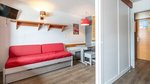 A room with a red sofa, a TV mounted on the wall, a wooden shelf, a red pendant light, and a door with a bulletin board. - Small, fully furnished studio for 4 people, with a balcony overlooking the ski slope (Tignes)