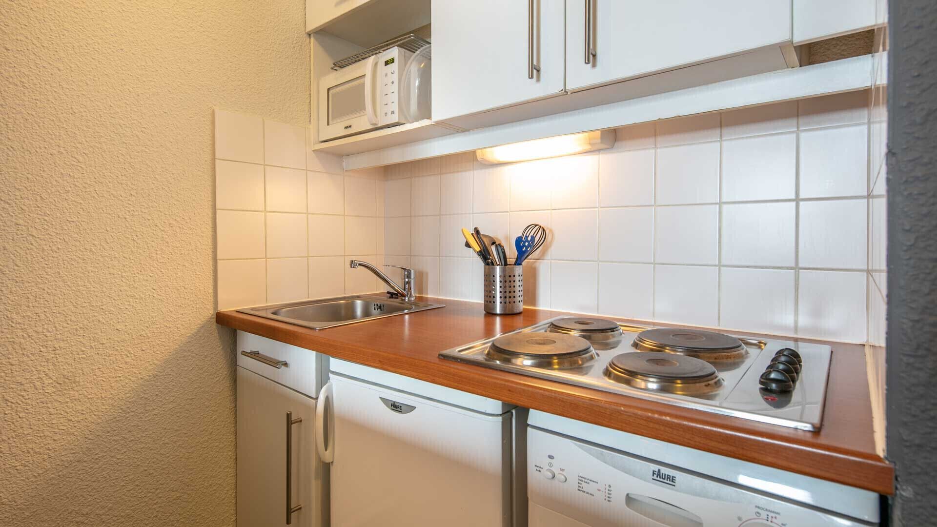 Et lille køkken med vask, komfur og mikroovn.