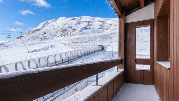 A wooden cabin with a snow-covered balcony overlooking a snowy mountain and ski lift. - Small, fully furnished studio for 4 people, with a balcony overlooking the ski slope (Tignes)