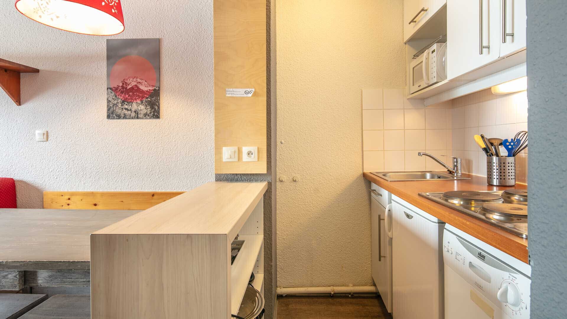 A compact kitchen with a wooden countertop, a built-in dishwasher, and a microwave above the sink.