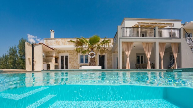 Una piscina con agua cristalina, un edificio de piedra con balcón y una palmera.