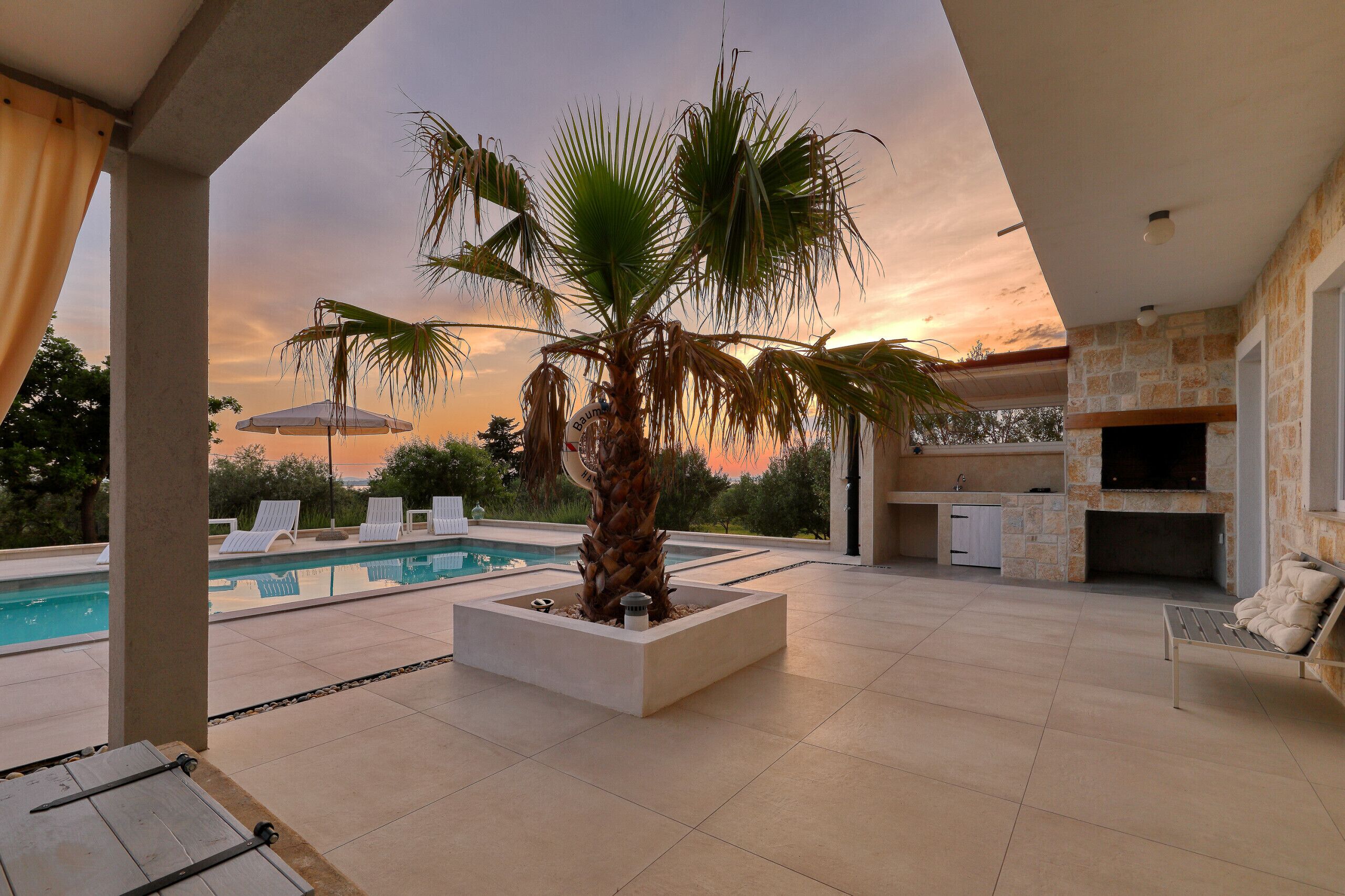 A poolside area with a palm tree, lounge chairs, and a stone fireplace.