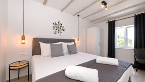 Un dormitorio con cama, mesita de noche, decoración en la pared y una ventana con cortinas.