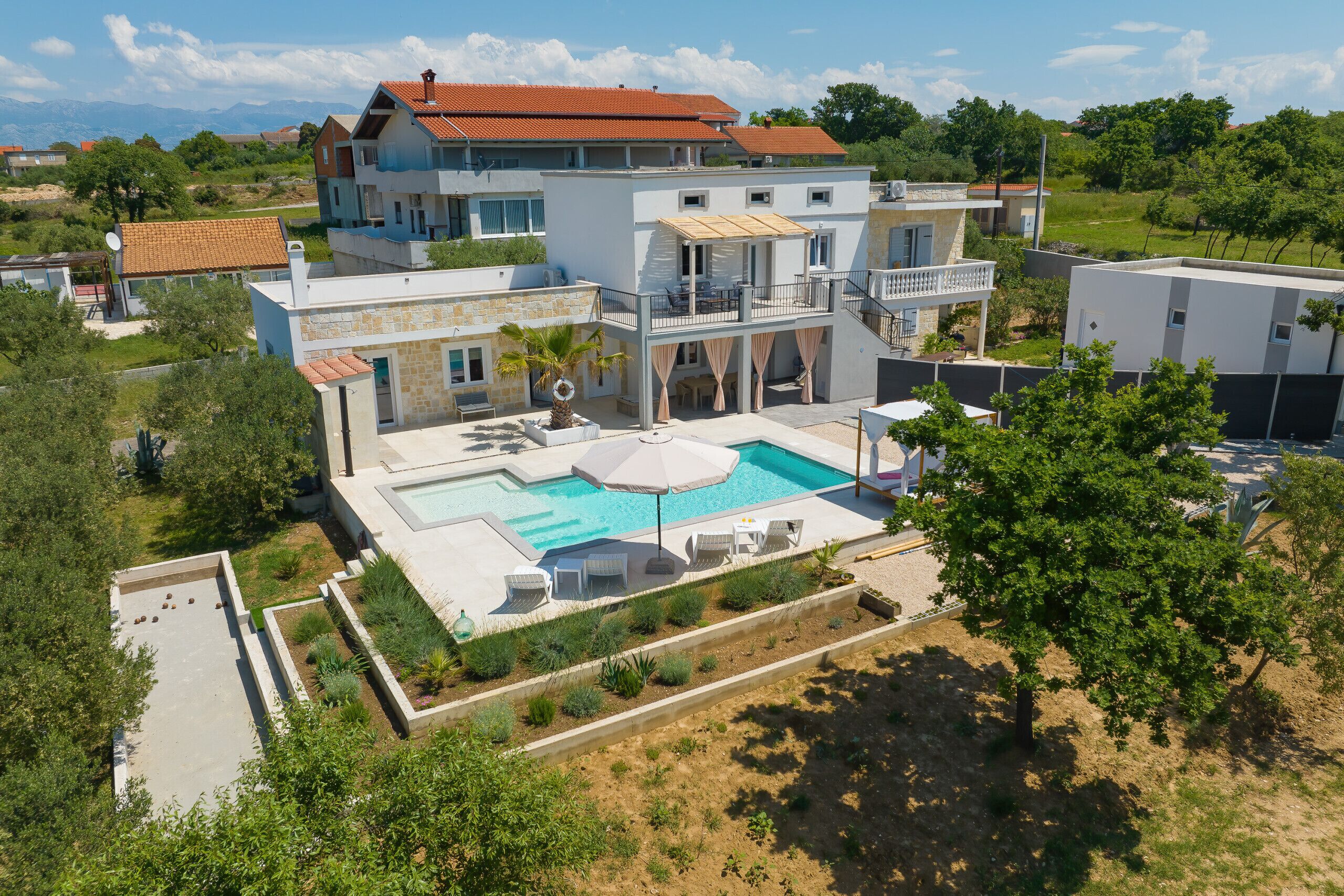 Una casa de varios pisos con piscina, mobiliario exterior y jardín.