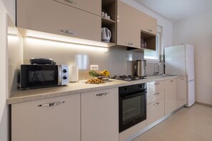 Eine moderne Küche mit Mikrowelle, Backofen und Kühlschrank, sowie einer Obstschale auf der Arbeitsplatte.