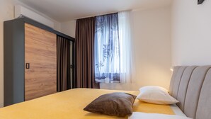 Un dormitorio con cama, almohadas, armario y ventana con cortinas.