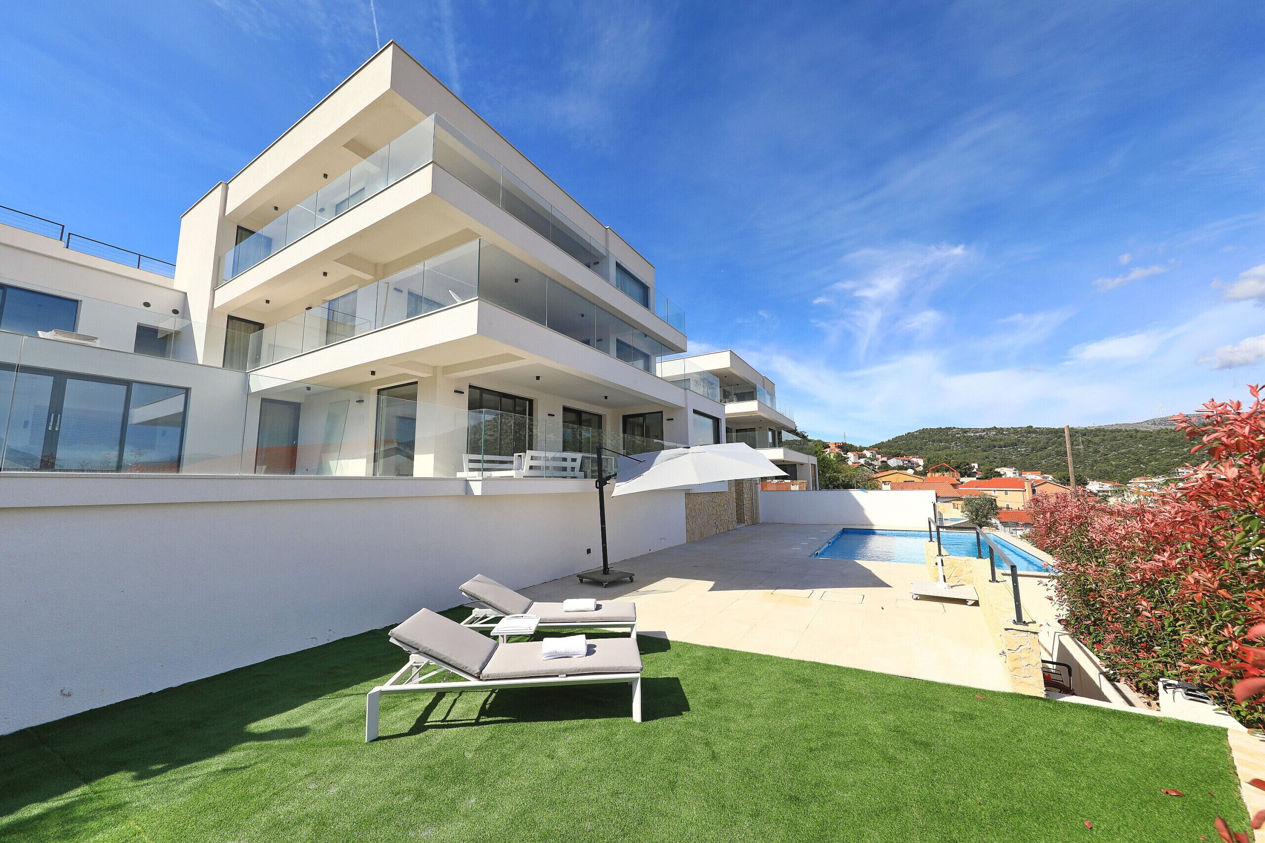 A modern multi-story building with a swimming pool, outdoor seating, and a well-maintained lawn.