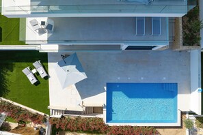 An aerial view of a modern house with a swimming pool, a patio with lounge chairs, and a garden. - Apartment Mentis with Sea View (Marina)