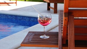Ein Glas rosa Getränk auf einem Holztisch am Pool.