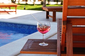 Ein Glas rosa Getränk auf einem Holztisch am Pool.