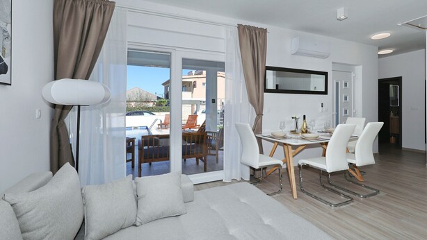 Ein modernes Wohnzimmer mit Sofa, Esstisch, Stühlen und Blick ins Freie.