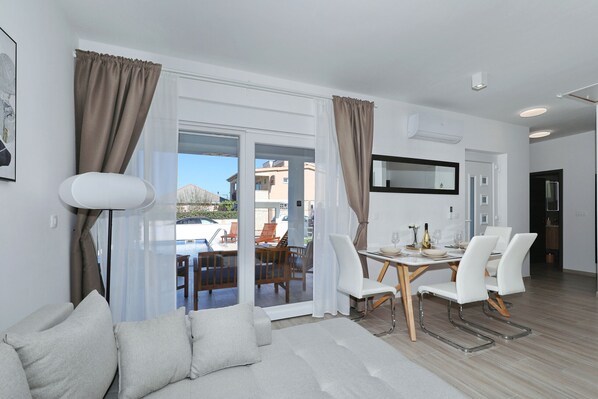 Ein modernes Wohnzimmer mit Sofa, Esstisch, Stühlen und Blick ins Freie.