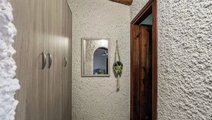 A narrow hallway with a wooden door, a textured wall, and a small mirror. - Monolocale in Villa (Porto San Paolo)