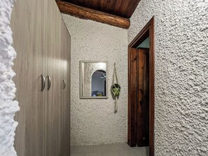 Um corredor estreito com porta de madeira, parede texturizada e um pequeno espelho.