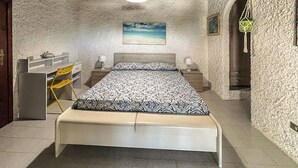 A bedroom with a bed, a desk, a chair, a painting, and a staircase. - Monolocale in Villa (Porto San Paolo)
