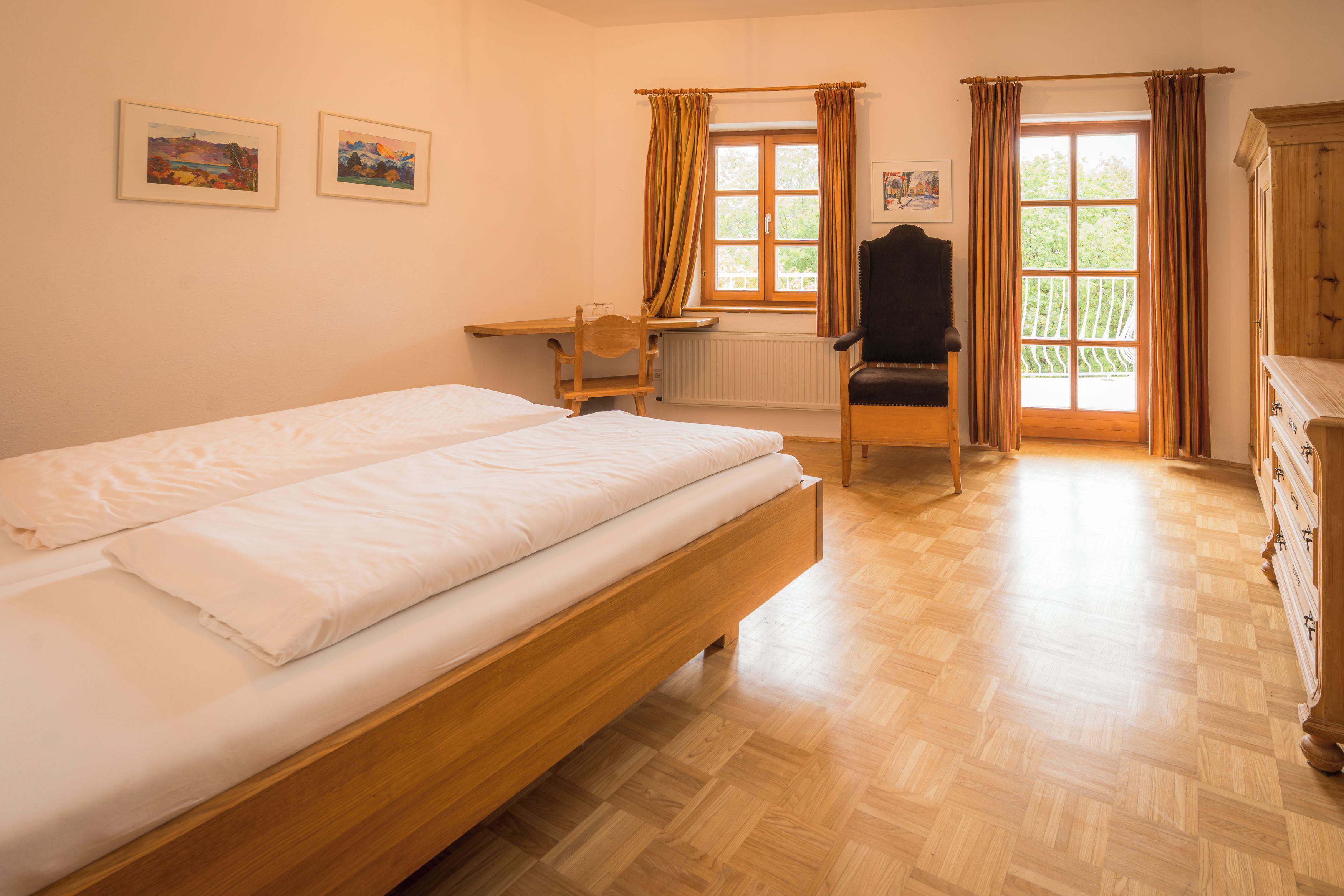 A bedroom with a wooden bed, a desk, and a chair. There are two framed pictures on the wall.