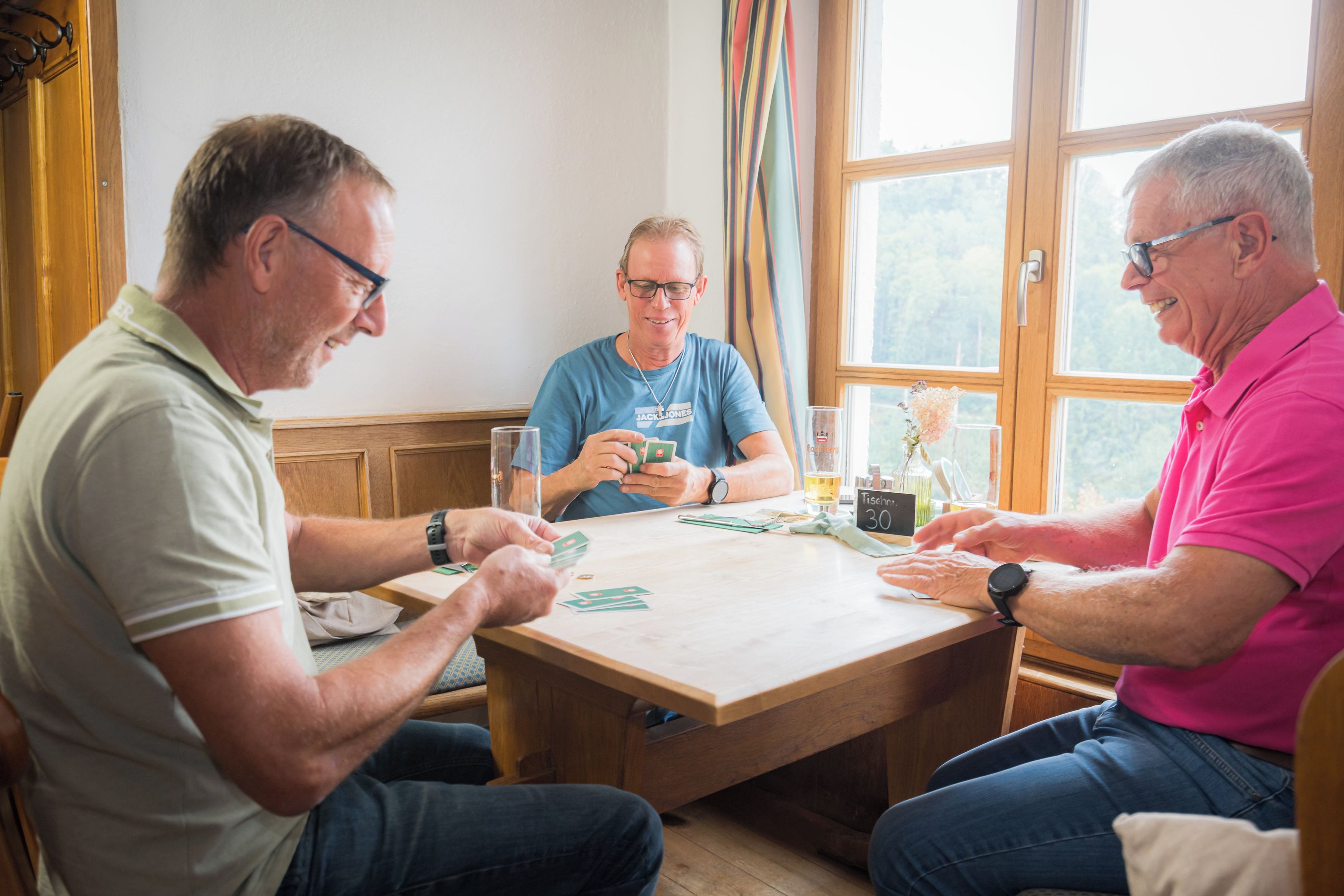 Three individuals seated at a wooden table with a window in the background.