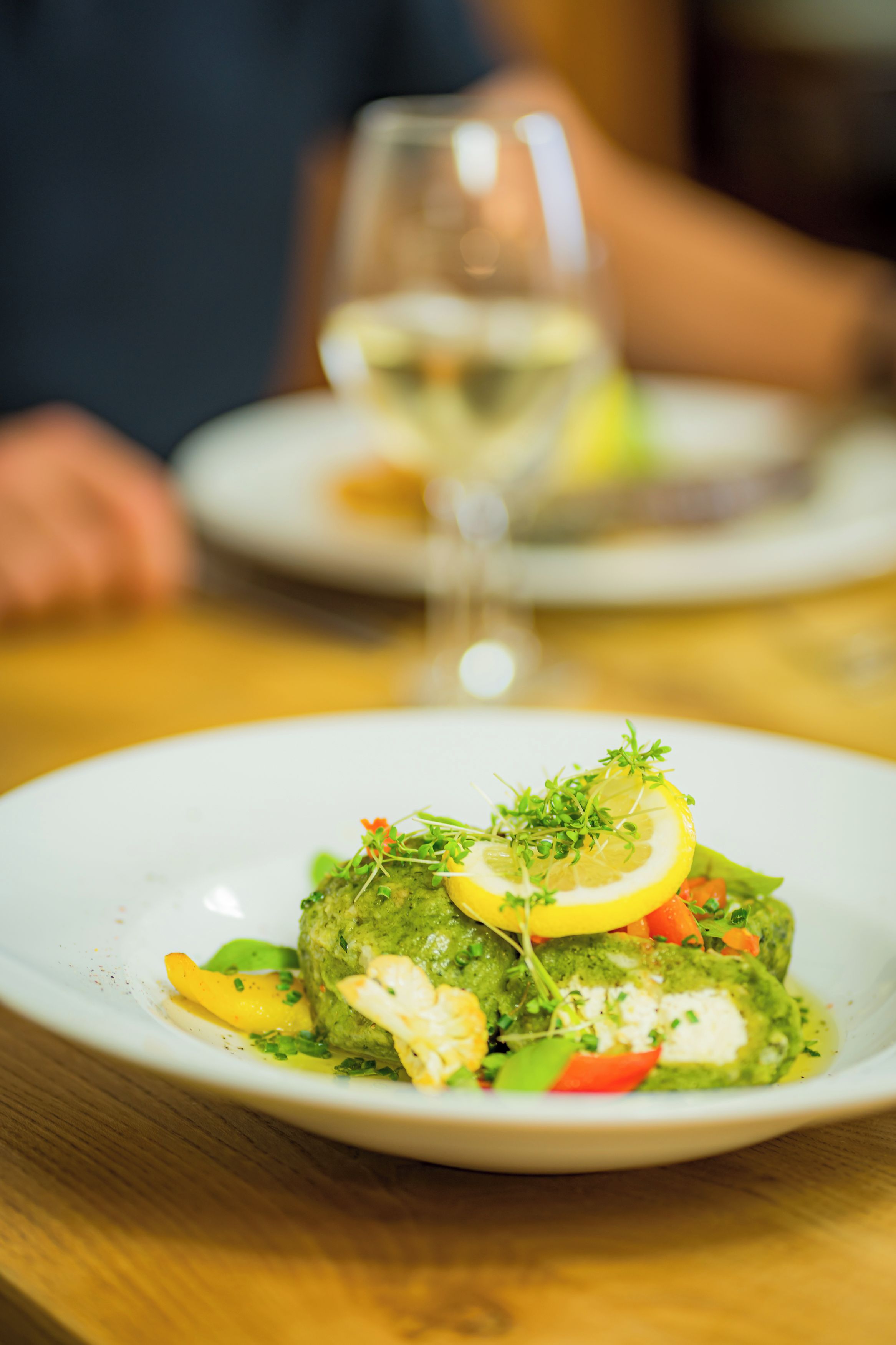 A plate of food with a green sauce, lemon, and vegetables.