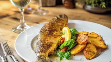 Prato com um peixe inteiro, batatas assadas e uma fatia de limão em um prato branco.