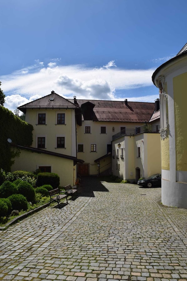 A cobblestone courtyard with buildings on either side, a bench, and a car parked on the right.