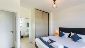A bedroom with a bed, a bedside lamp, a wardrobe, and a bathroom visible through an open door. - Atea Pearl (Pirae)