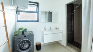 A modern bathroom with a washing machine, a sink, a mirror, and a shower. - Atea Pearl (Pirae)