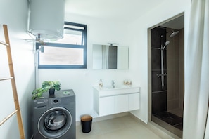 A modern bathroom with a washing machine, a sink with a mirror, and a shower. - Atea Pearl (Pirae)
