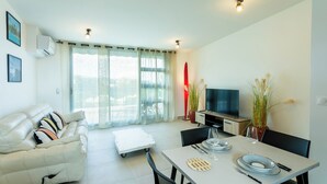 A modern living room with a sofa, dining table, TV, and potted plants. - Atea Pearl (Pirae)